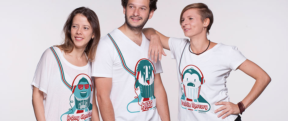 Das Bild zeigt drei Personen. Zwei Frauen und ein Mann. Alle tragen das T-shirt mit dem T-shirt Design von fraganzy. Das Design am T-Shirt zeigt eine Illustration in blau und rot von einem Cupcake. Jeder Cupcake hat das Gesicht einer berühmten Person. Die Frau auf der linken Seite trägrt das T-Shirt mit dem Cupcake Design des Musikers Ray Charles. Der Mann in der Mitte trägt das T-Shirt mit dem Cupcake Design des Sängers von der Rockband KISS. Und die Frau auf der rechten Seite trägt das T-Shirt mit dem Cupcake Design von Freddie Mercury.